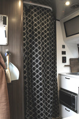 Compact RV rental interior showing a black patterned shower curtain, kitchen sink, and built-in microwave unit.