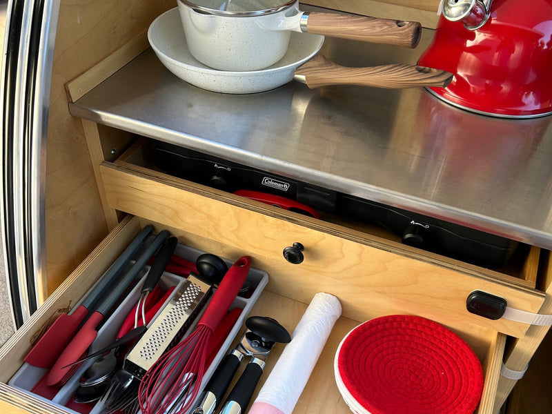  being accessed by a hand.|Inside a compact RV rental: a cozy bed with red plaid blanket — photo 7