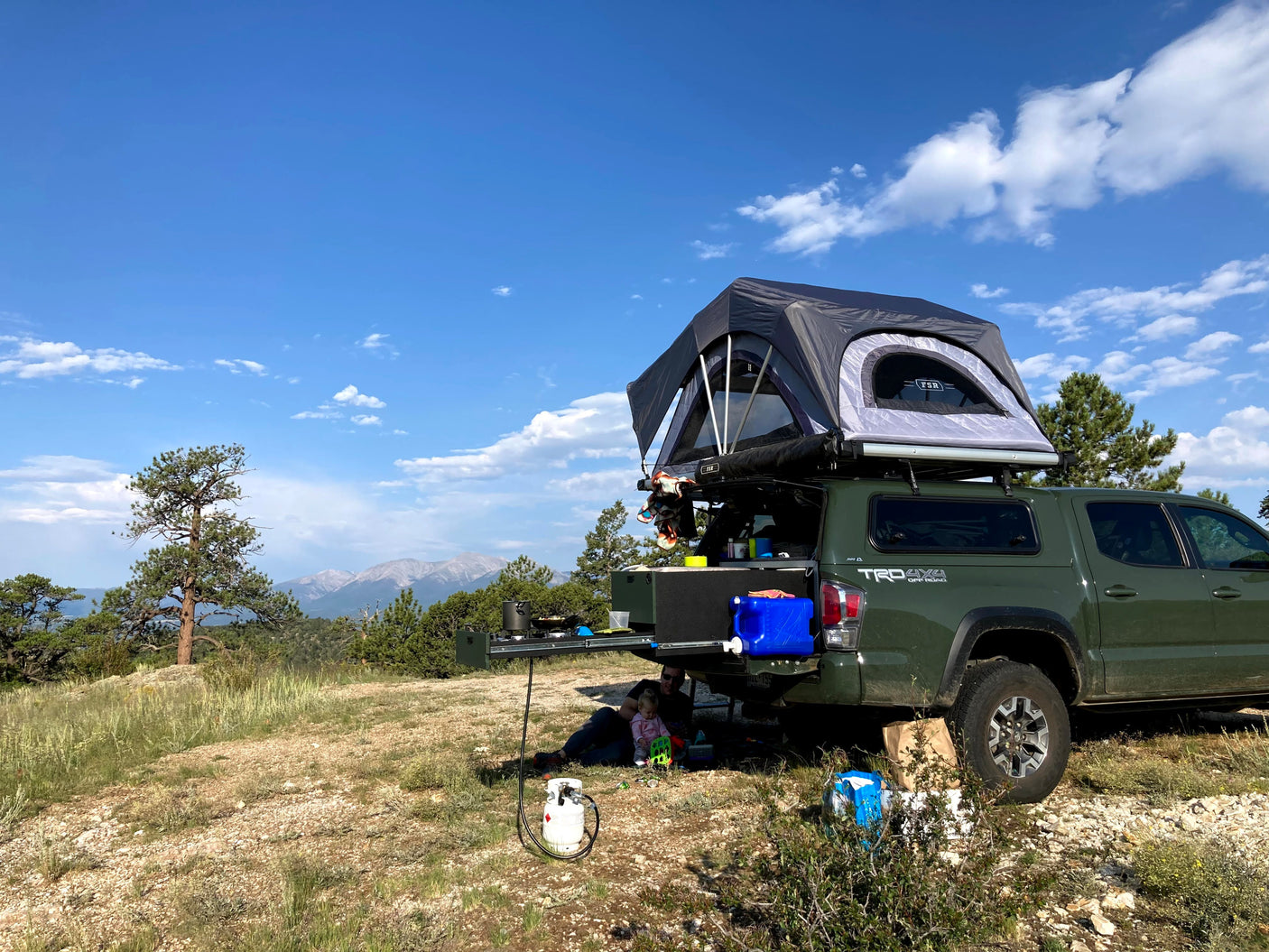 Experience overlanding! This truck with a rooftop tent and slide-out kitchen is perfect for an RV rental adventure, with mountains in the background.