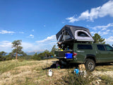 Experience overlanding! This truck with a rooftop tent and slide-out kitchen is perfect for an RV rental adventure, with mountains in the background.