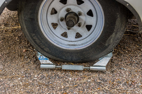 An RV rental tire is securely chocked on gravel with a BAL locking chock, ensuring stability and preventing movement.