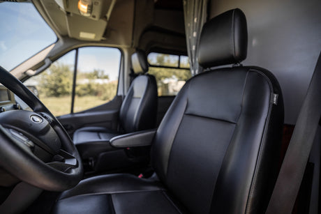 Explore this RV rental's inviting front cabin. View black leather seats & steering wheel, ready for your adventure.