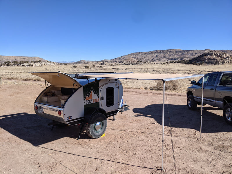An RV rental teardrop camper (RockyTrax) with an open galley & awning, beside a pickup in a dry, sunny desert. Ideal for outdoor adventures. — photo 4