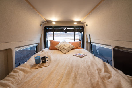 Wake up to stunning views in this cozy rv rental. Comfortable bed inside a camper van, overlooking a scenic lake.