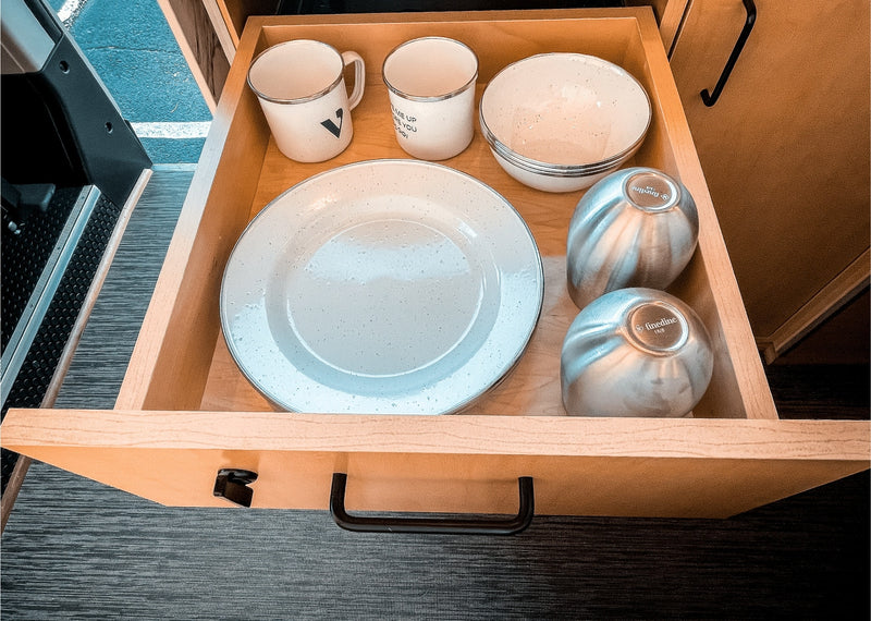  a grey saucepan rests on an induction cooktop on a white marble-look counter. Sink and cozy bed visible.|Step inside this RV rental's cozy interior — photo 14