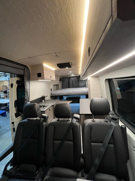 Interior of an RV rental: View from front shows black leather seats, bright LED lighting, and a spacious living area.