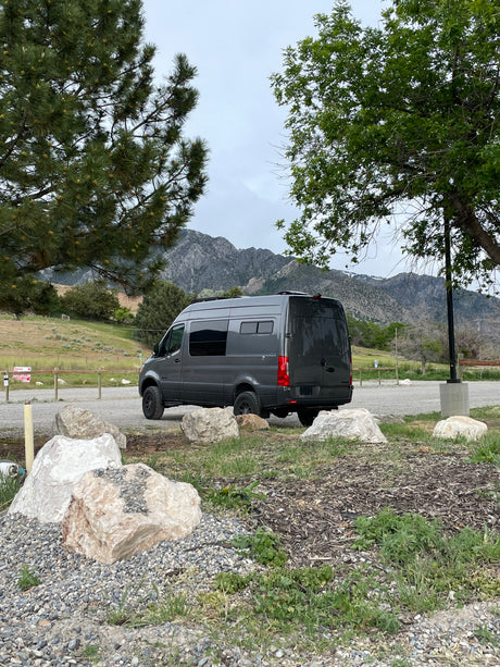 A dark gray camper van in a mountain park setting, ready for adventure. Ideal for rv rental.