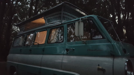 Cozy vintage pop-top RV rental parked in a dark forest, interior lights glowing. Your next camping adventure awaits!
