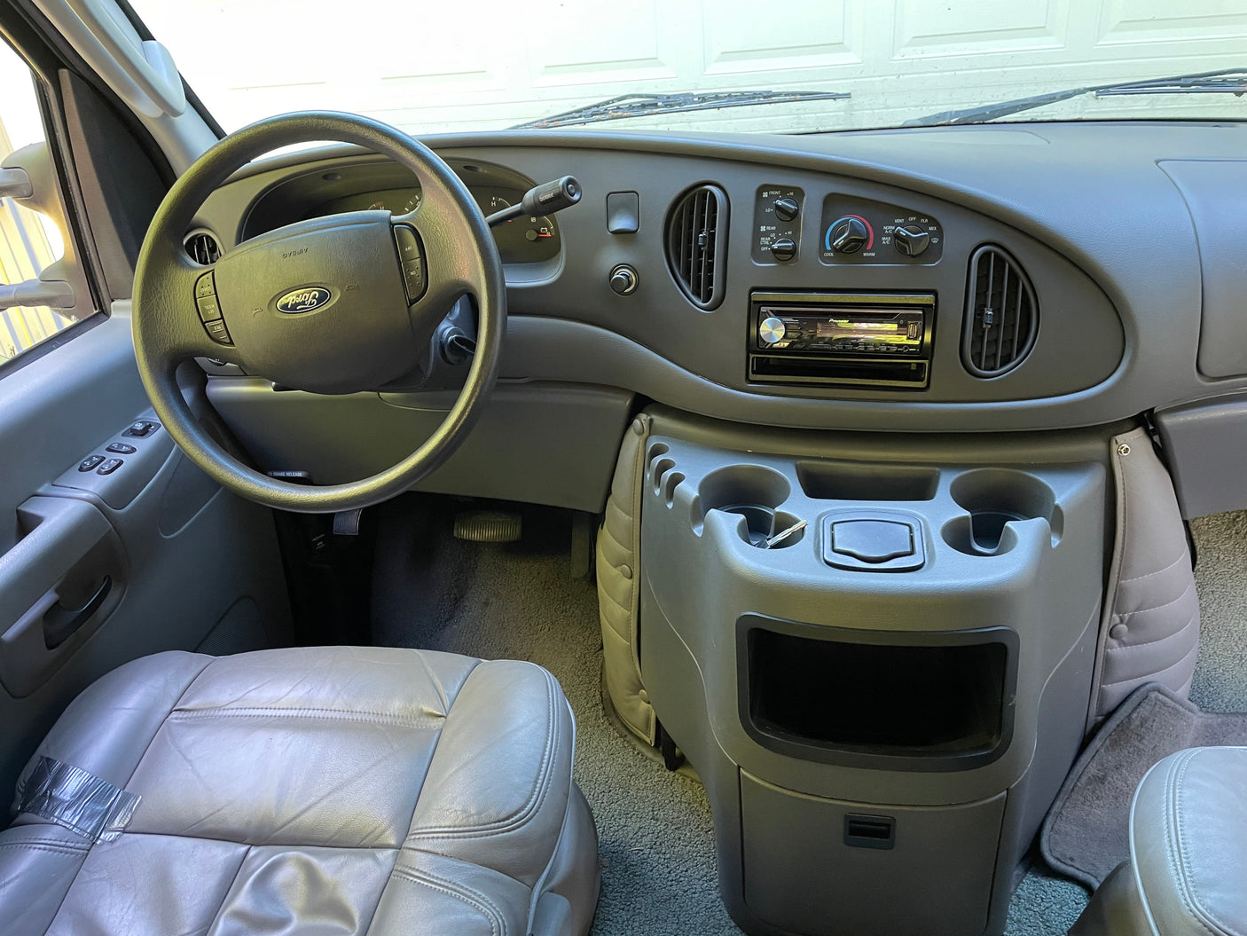 RV rental cockpit view: Ford steering wheel, dashboard with climate controls, Pioneer stereo, cupholders, & driver's seat.