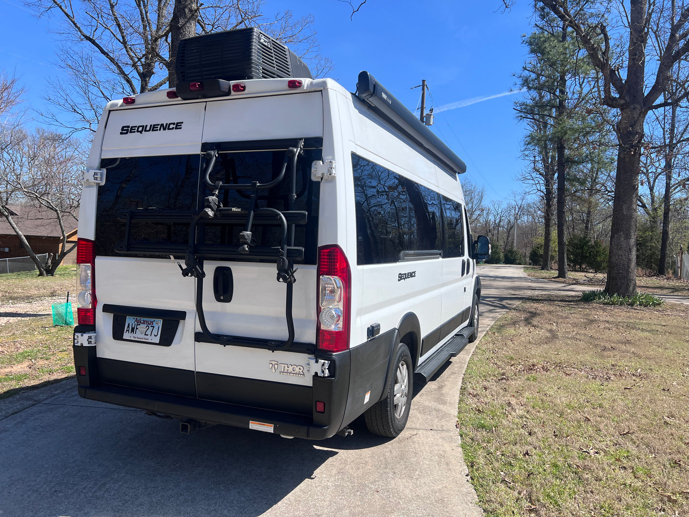White Thor Sequence RV rental, equipped with a bike rack and roof AC unit, parked on a paved driveway on a sunny day.