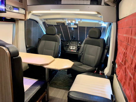 Interior of an RV rental camper van, showing swiveling front seats, a central table, and comfortable living area seating.
