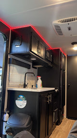 This RV rental's modern interior features a sleek kitchen with red LED accent lighting, black cabinetry, and appliances.