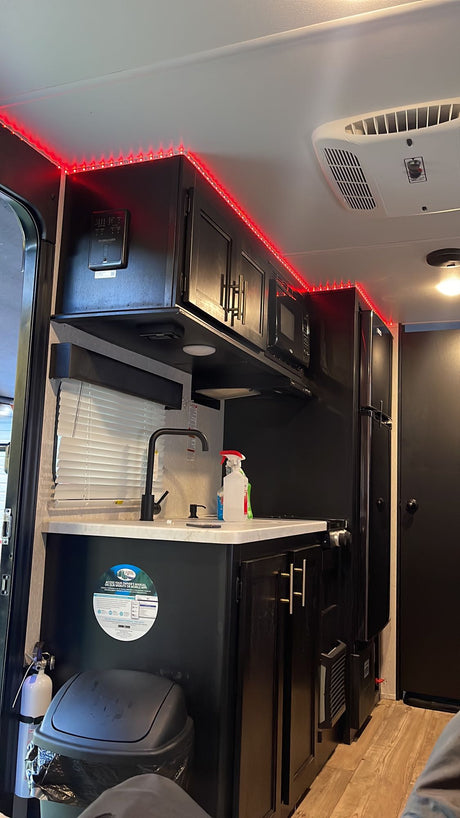 This RV rental's modern interior features a sleek kitchen with red LED accent lighting, black cabinetry, and appliances.