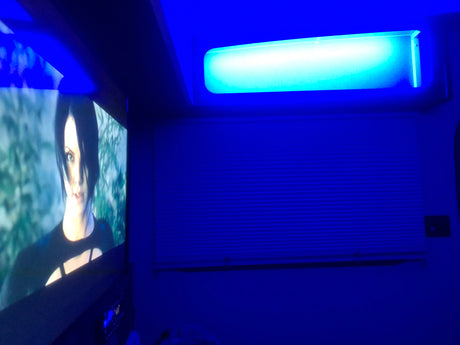 RV rental interior with striking blue ambient lighting, a screen showing a video game, and horizontal window blinds.