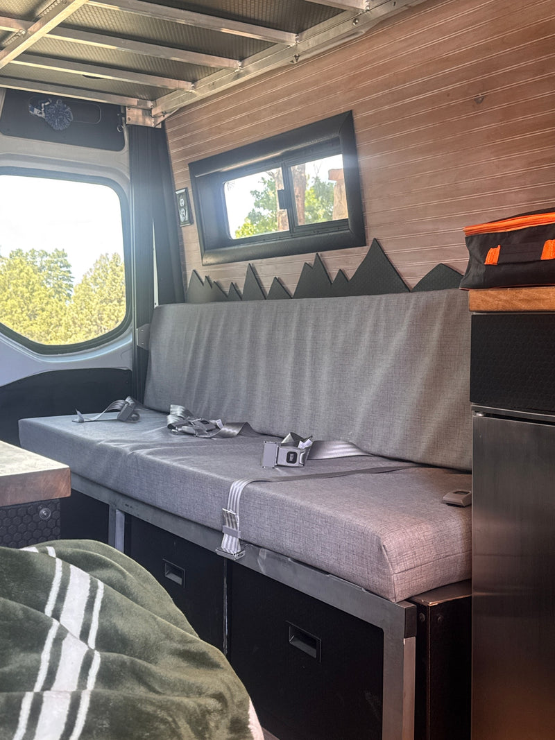 Relax in this RV rental's comfy grey bench, featuring seatbelts, wood-paneled walls, mountain decor, and outdoor views. — photo 3