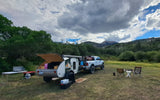RV rental: Teardrop camper & truck camping setup in a lush mountain valley under cloudy skies, perfect for adventure!