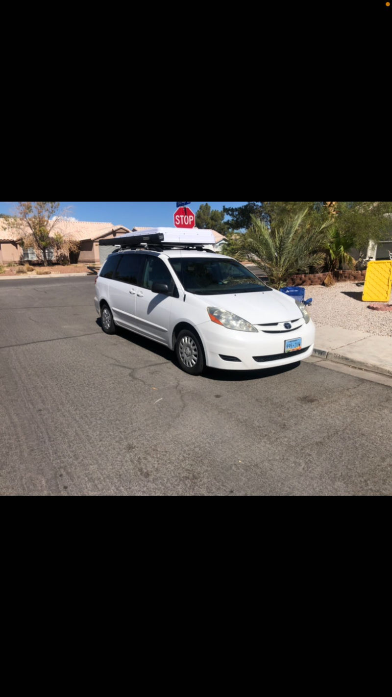  parked with camping chairs on a sunny street.|A white minivan with a brown rooftop tent — photo 8