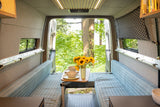 Enjoy nature from this rv rental! Cozy camper van interior with dining, striped benches, and open forest views.