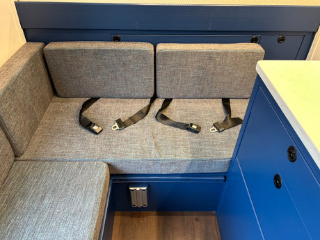 RV rental interior: Gray upholstered bench seating with two black seatbelts, blue cabinetry, and a light countertop.