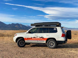 White Titus Adventure Co. overland SUV (like an RV rental) with awning, mountains in background.