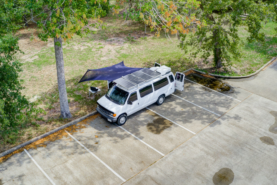 Overhead view of an RV rental camper van with solar panels, open doors, and a shaded outdoor office setup.