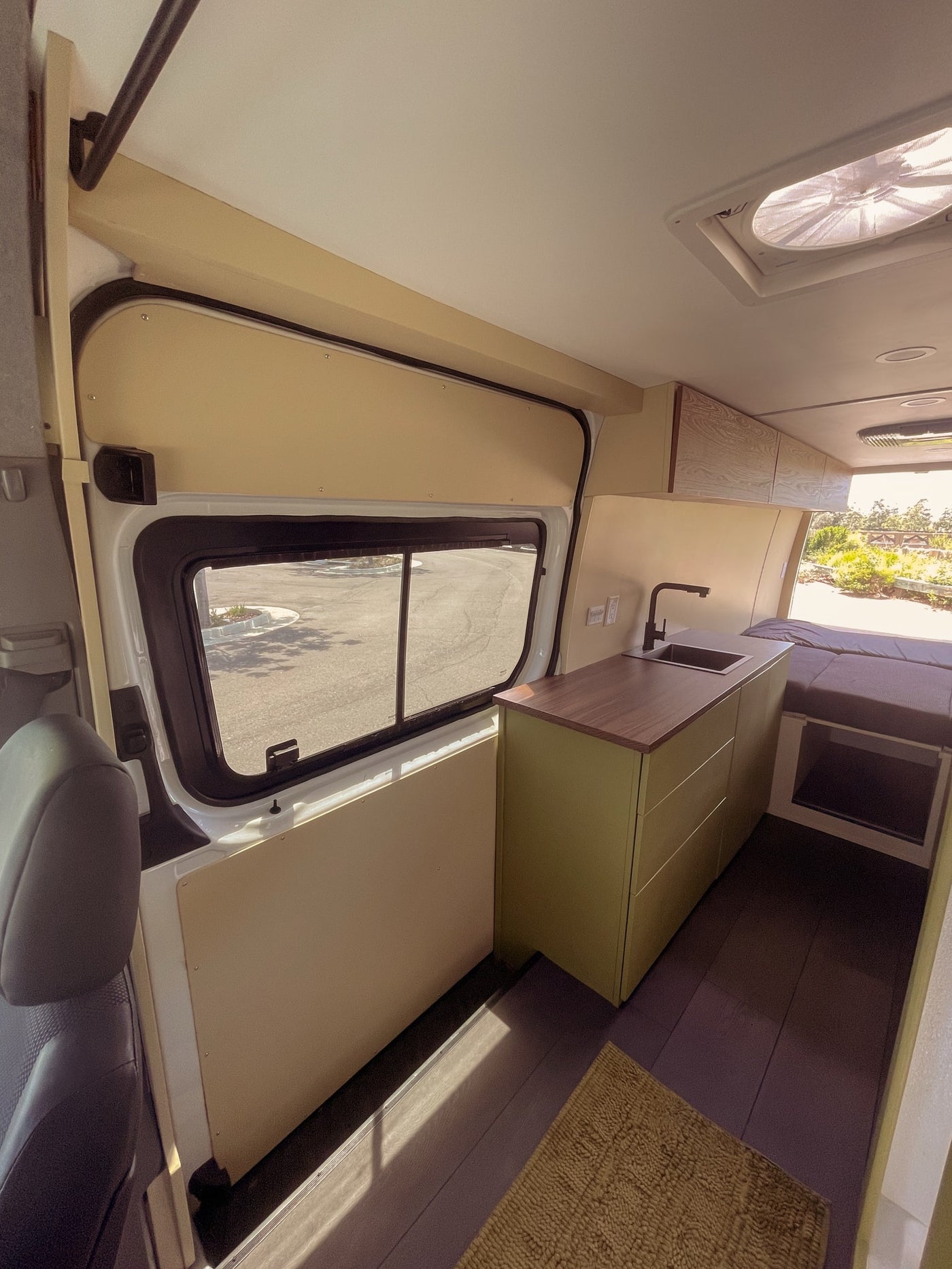 Inside an RV rental: a modern camper van interior with a sleek kitchenette, green cabinets, and a cozy bed. Views from the large window. — photo 13