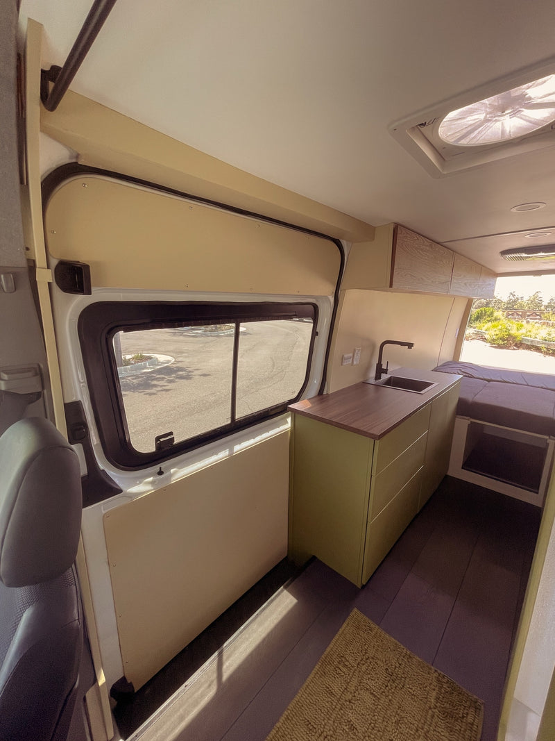 Inside an RV rental: a modern camper van interior with a sleek kitchenette, green cabinets, and a cozy bed. Views from the large window. — photo 13