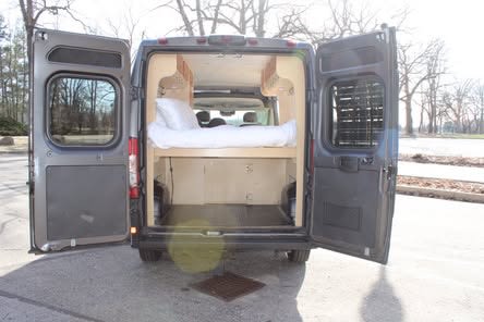 This RV rental camper van interior, with open rear doors, shows a bed with storage below, perfect for mobile living.