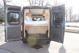 This RV rental camper van interior, with open rear doors, shows a bed with storage below, perfect for mobile living.