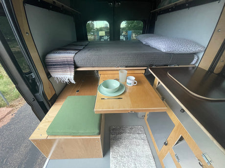 Cozy campervan interior for your next rv rental adventure, featuring a bed, dining area, and compact kitchen setup.