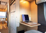 Modern RV rental interior with a dedicated workspace, featuring a laptop on a light wood desk. Ideal for remote work while traveling.