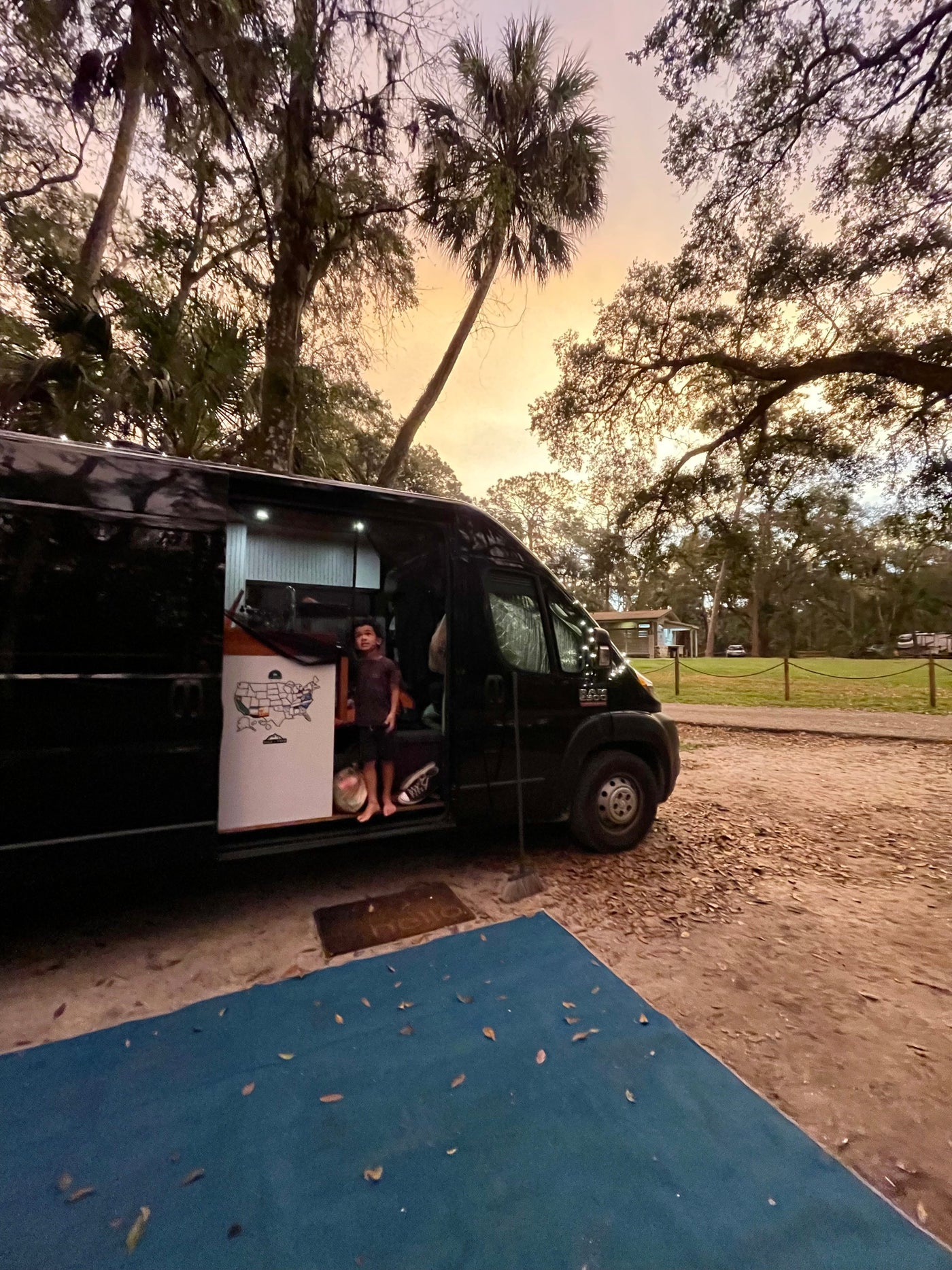 Scenic RV rental camping at sunset. A child is visible inside the black camper van, parked amidst trees. — photo 8