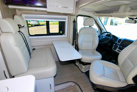 Bright and airy rv rental interior featuring cream leather seats, a movable table, and a TV for travel comfort.
