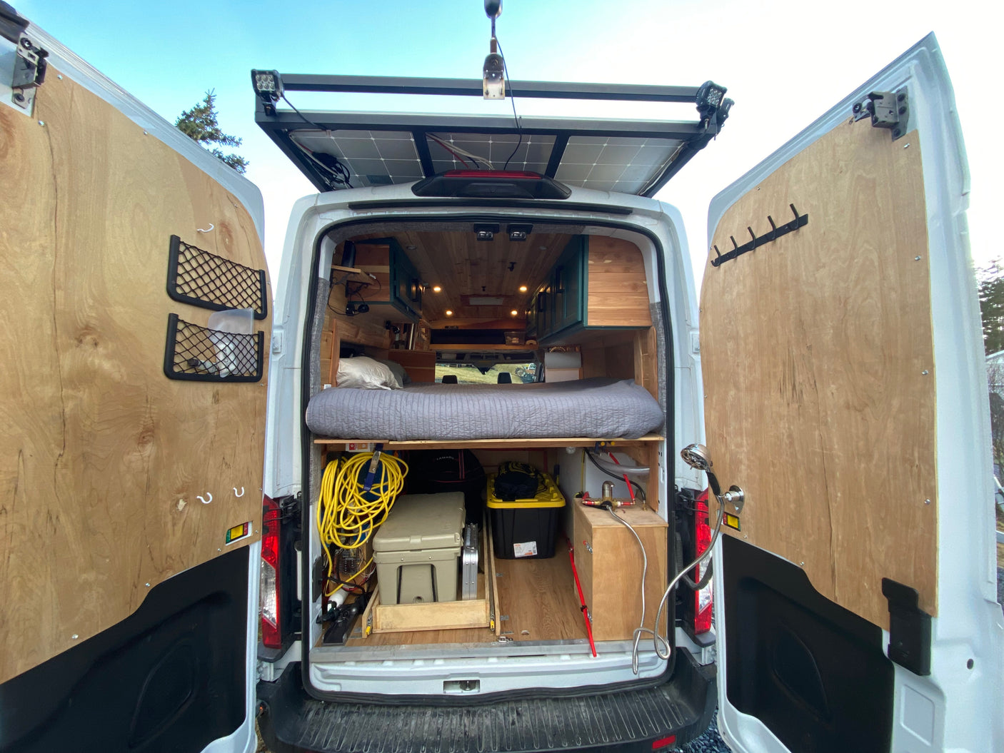 Experience mobile living in this rv rental camper van: rear view shows cozy bed, ample storage, solar power, & outdoor shower.