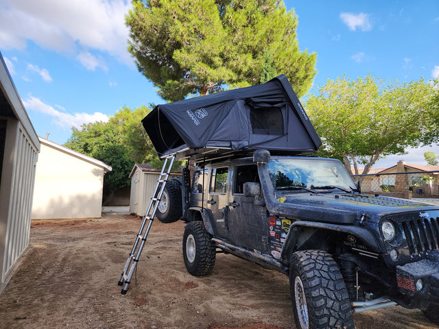 Black iKamper Skycamp 3.0 hardshell rooftop tent opened on a Jeep Wrangler Unlimited with the telescoping ladder extended