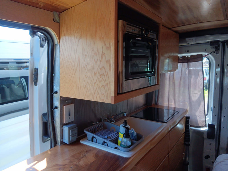 Compact RV rental kitchen features microwave, sink, and cooktop in a custom van conversion, perfect for travel. — photo 8