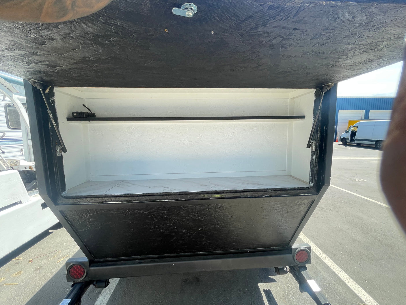 Opened rear utility box on an RV rental, featuring a shelf and power outlet for convenient mobile storage.