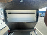 Opened rear utility box on an RV rental, featuring a shelf and power outlet for convenient mobile storage.