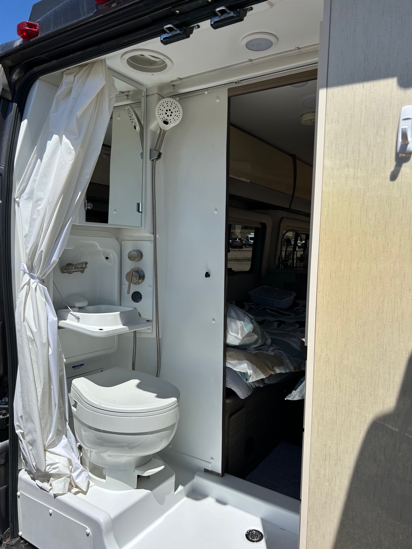 Inside an RV rental: a compact wet bath with toilet, foldable sink, and shower, adjacent to the bed.