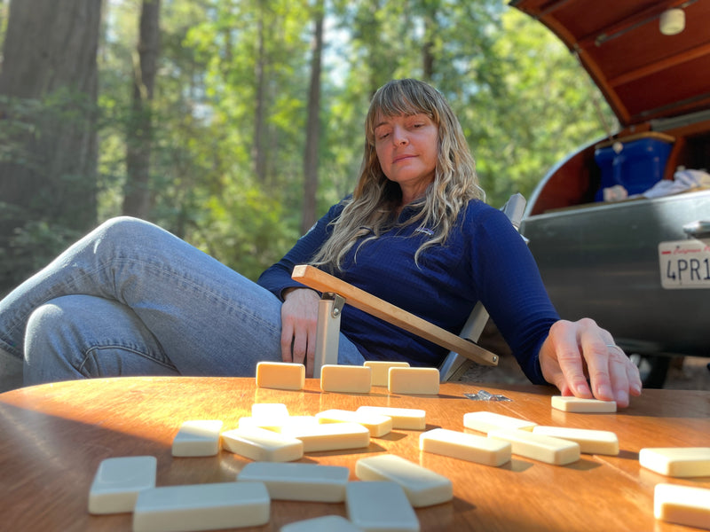 Woman playing tiles on wooden table at RV rental camp, relaxing outdoors with trees in background. — photo 12