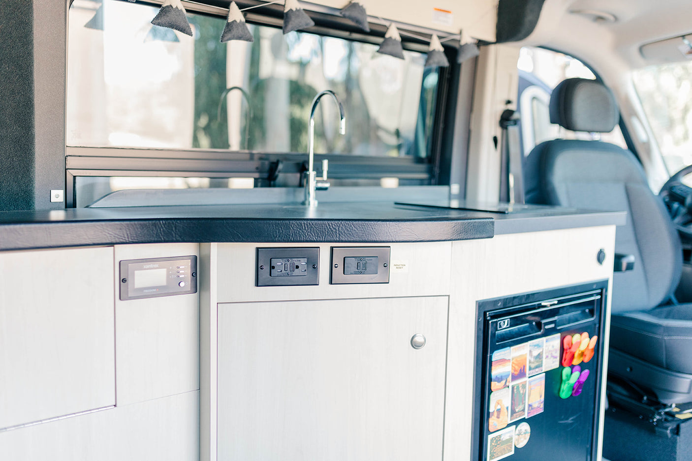 Explore this RV rental's equipped kitchen: sink, induction point, fridge, and Xantrex power panel. Comfort on the road.