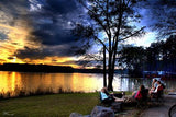 Friends relax at a lake sunset. RV rental makes tranquil lake camping possible. RVs visible across the water.