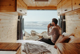 Relaxing in an RV rental! Man sips coffee with stunning ocean views from his cozy, wood-paneled camper van.