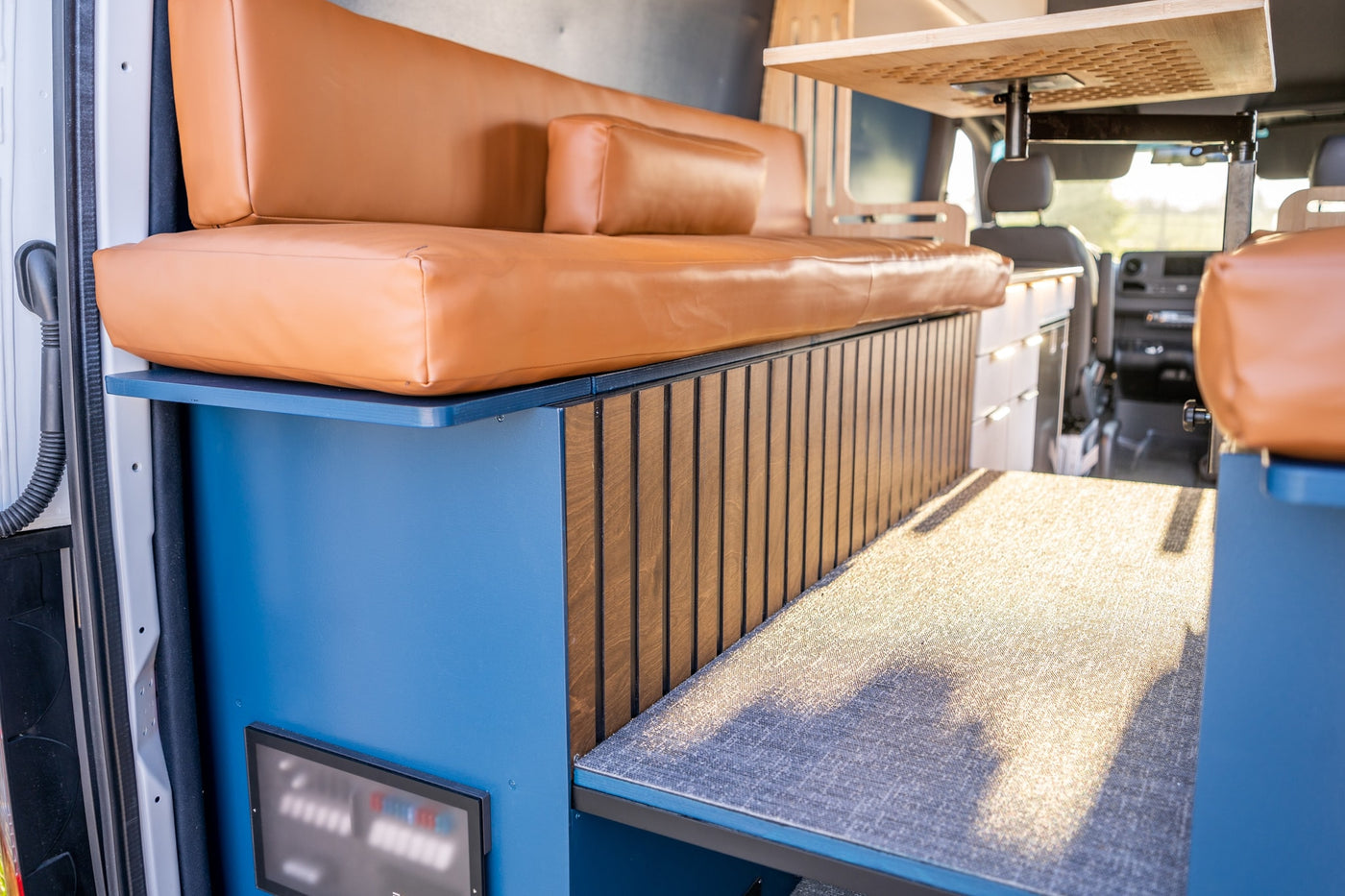 Modern **rv rental** camper interior with a plush tan sofa, blue base, wood slats, and a floating table for comfortable travels. — photo 9