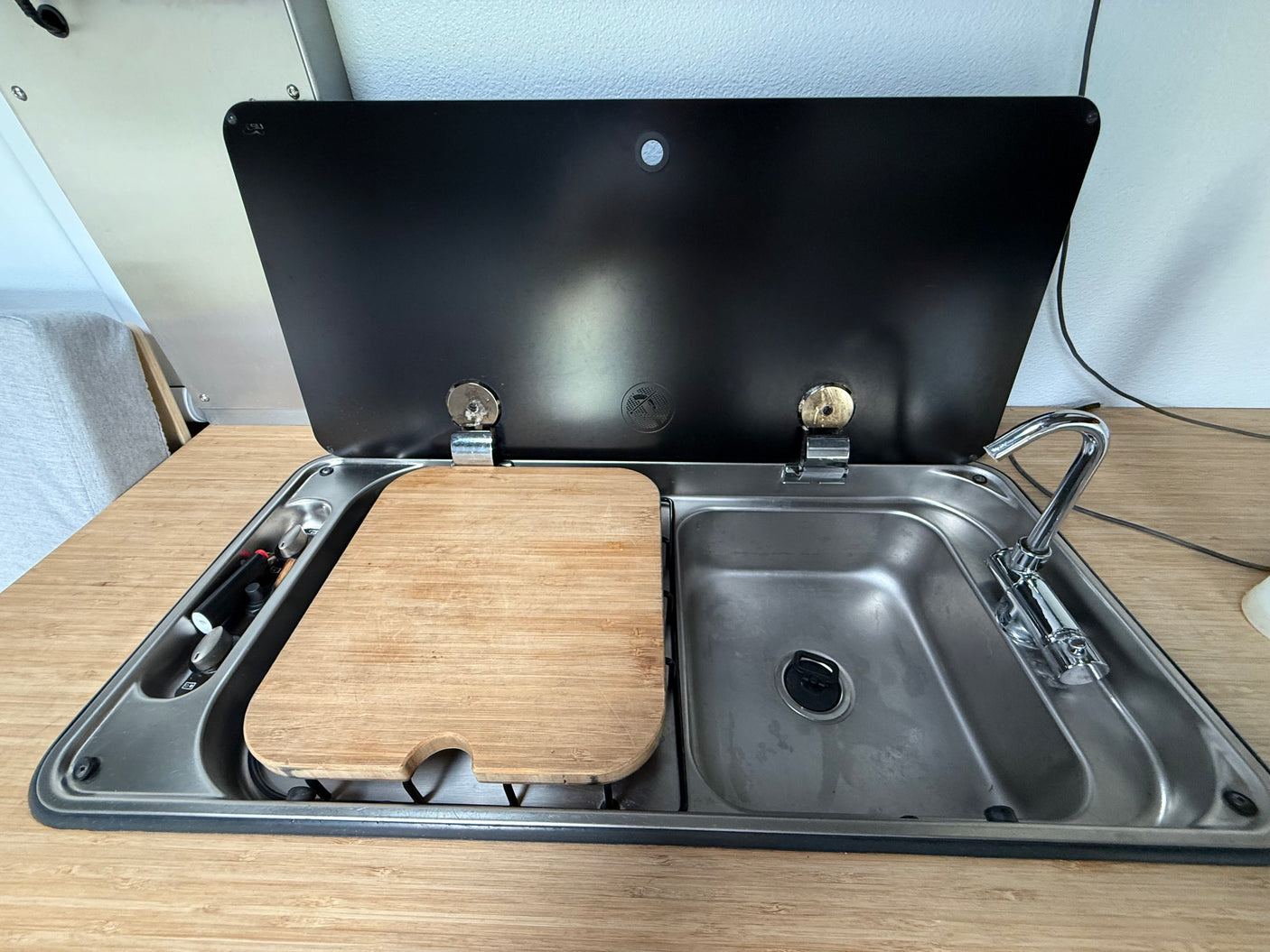 RV rental kitchen: Stainless steel sink, chrome faucet, and wooden cutting board covering the stove unit.