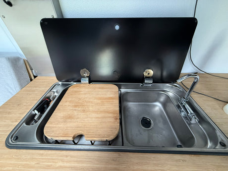 RV rental kitchen: Stainless steel sink, chrome faucet, and wooden cutting board covering the stove unit.