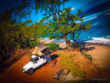 Coastal adventure! A white Jeep with a rooftop tent, a unique RV rental choice, perfectly set for beach camping by the ocean.