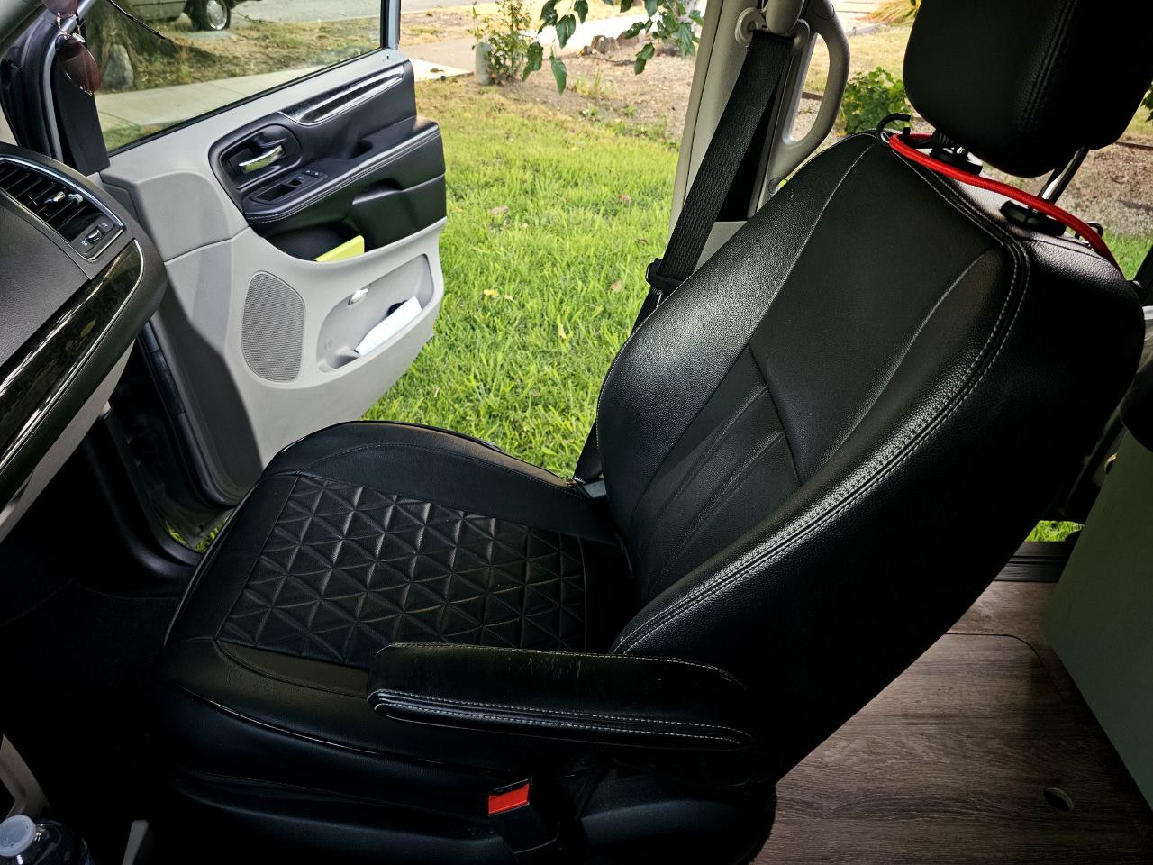 RV rental interior: Black quilted leather seat & open door revealing green grass.