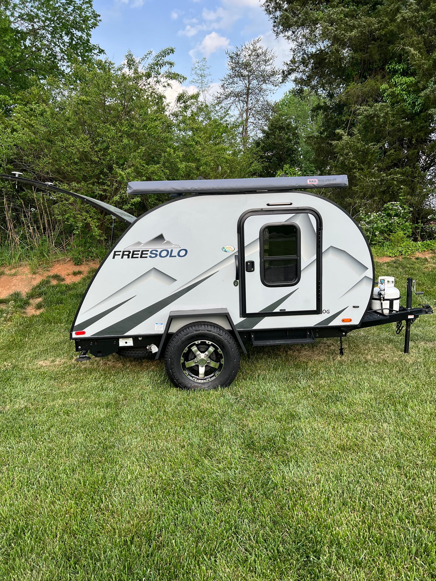 This Freesolo teardrop camper RV rental is grey with black accents, an awning, and propane tank. Parked on green grass.