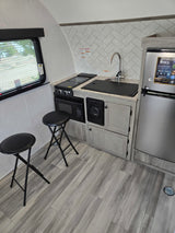Modern RV rental galley featuring a compact kitchen with a sink, stovetop, microwave, fridge, and two bar stools.